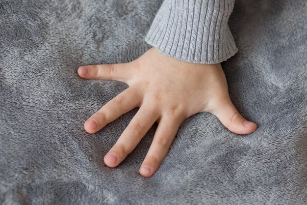 Foto la mano de un niño sobre un fondo gris la mano de una niña con los dedos extendidos sobre un tejido de felpa gris