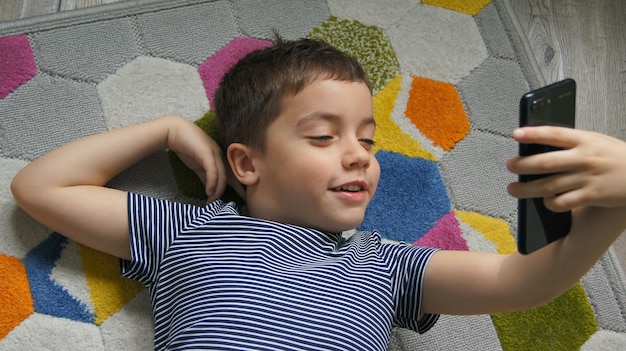 Mano de niño sonriente sosteniendo teléfono móvil o teléfono inteligente haciendo selfie retrato foto o video llamada conferencia