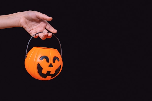 Foto mano del niño sosteniendo una canasta de calabaza naranja, jack lantern aislado sobre fondo negro. esperando caramelos de halloween. tradición de truco o trato. feliz concepto de halloween