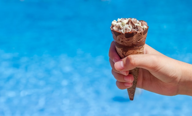 Mano de niño sosteniendo un helado de chocolate en cono de oblea cerca de la piscina