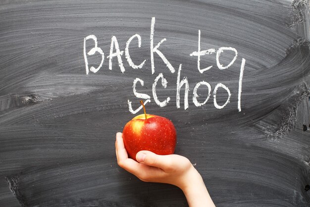 Mano del niño sosteniendo una manzana cerca de una pizarra