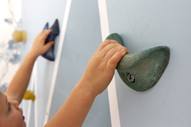 La mano del niño se sujeta firmemente al gancho del muro de escalada azul.