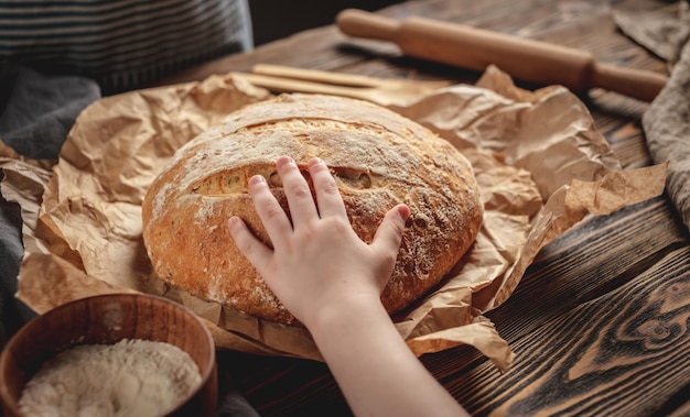 La mano de un niño toca pan fresco natural hecho en casa con una corteza dorada en una servilleta sobre un fondo de madera antiguo