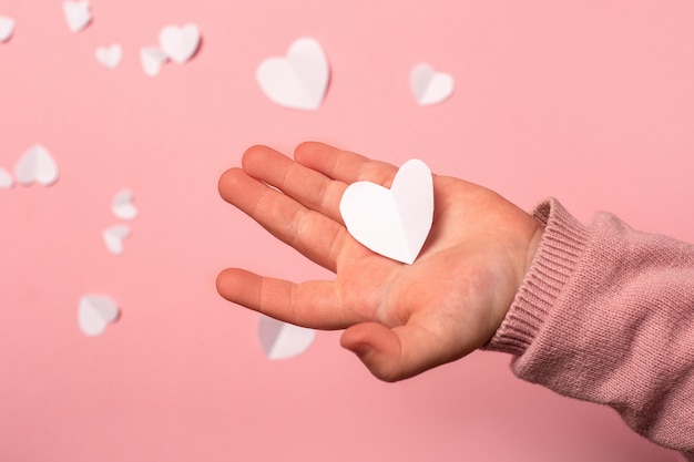 La mano del niño toma una tarjeta de San Valentín de papel sobre un fondo rosa. Composición de San Valentín. Bandera. Vista plana endecha, superior.