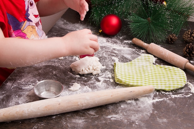 Mano de niños hace galletas para Navidad, año nuevo, fondo de madera, rodillo sobre la mesa, masa en harina, lugar de copia