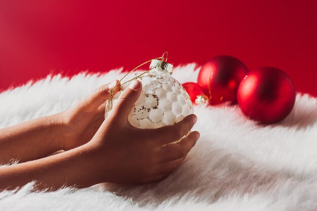 La mano de los niños sostiene una decoración de bolas blancas de Navidad contra