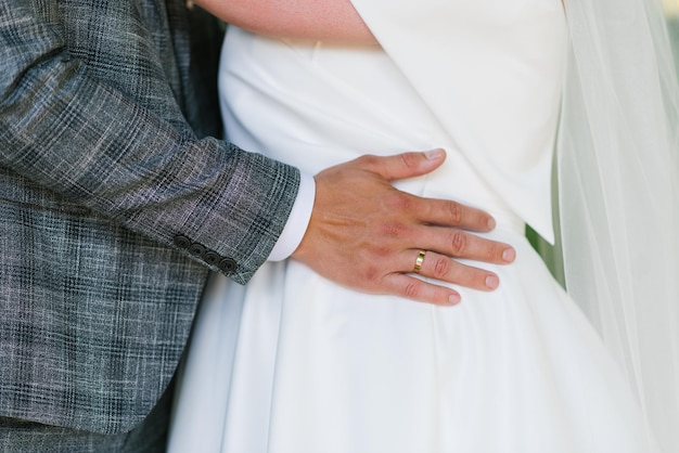 La mano del novio con el anillo de bodas se encuentra en la cintura de la novia.