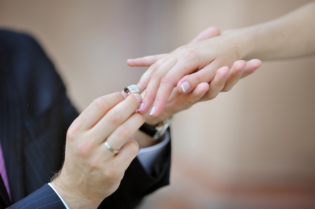 La mano del novio poniendo un anillo de bodas en el dedo de la novia