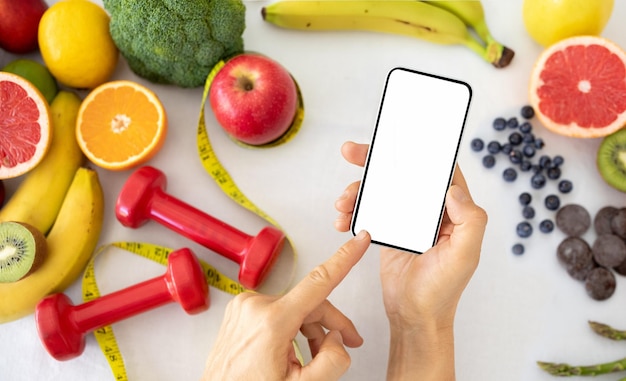 La mano de un nutricionista caucásico muestra un plan de pérdida de peso por teléfono con pantalla en blanco en la mesa con