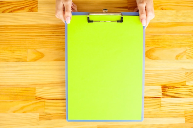 Mano de oficina sosteniendo una carpeta con un papel de color verde en el fondo de la mesa de madera