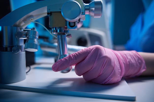 La mano operando un micromanipulador junto a un microscopio