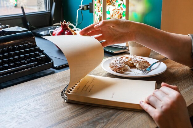 Mano con organizador de cuaderno de papel en la mesa de madera del escritorio de la cafetería mirando a través de los planes de tareas