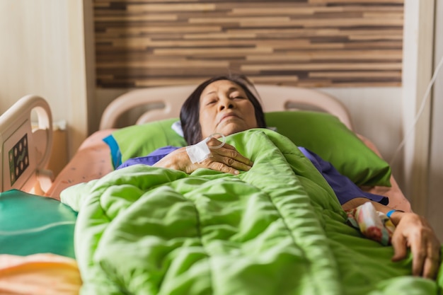 Mano del paciente mayor con inyección de solución salina en la cama del hospital