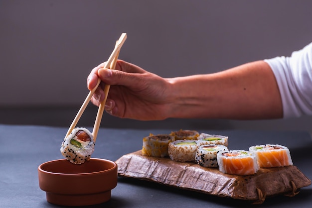 Mano con palillos sumergiendo sushi en salsa de soja