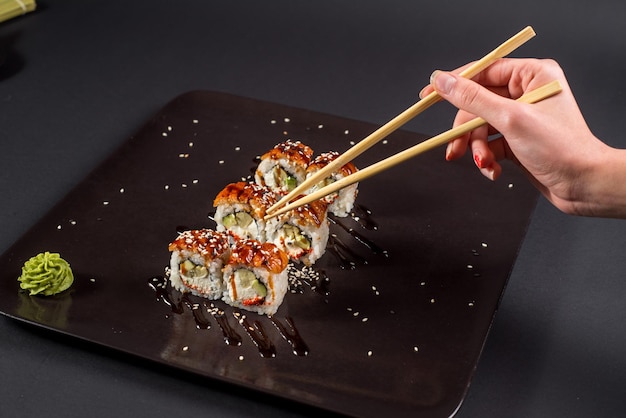 Mano con palillos para sushi tomando un rollo sobre fondo oscuro