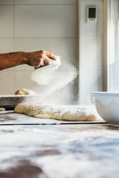 Mano de panadero extendiendo la harina a la masa. Concepto de panadería.