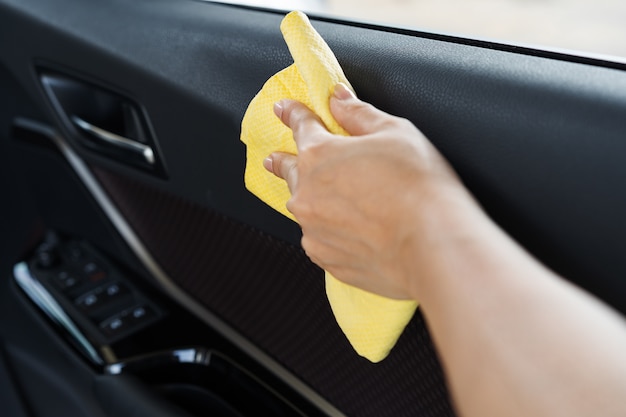 Mano con paño de microfibra limpiando la puerta interior del coche