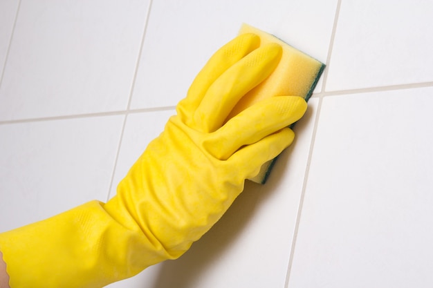 De la mano en la pared de azulejos de limpieza de guante amarillo