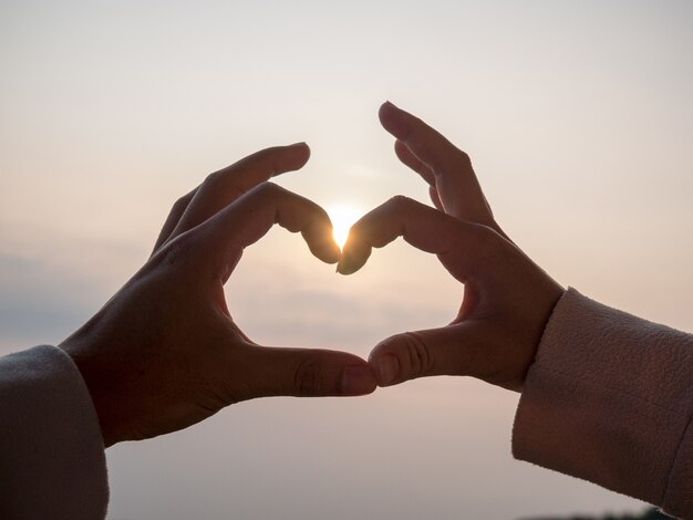 La mano de la pareja tiene forma de corazón. Entre el fondo del cielo y el sol