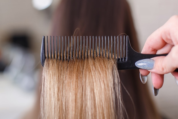 Mano del peluquero cepillando el cabello largo morena en salón de belleza