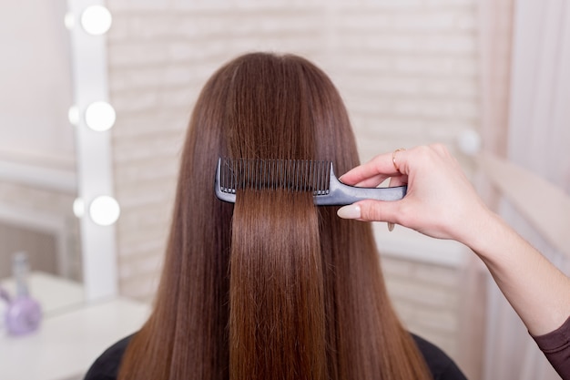 Mano de peluqueros cepillarse el pelo largo morena en salón de belleza