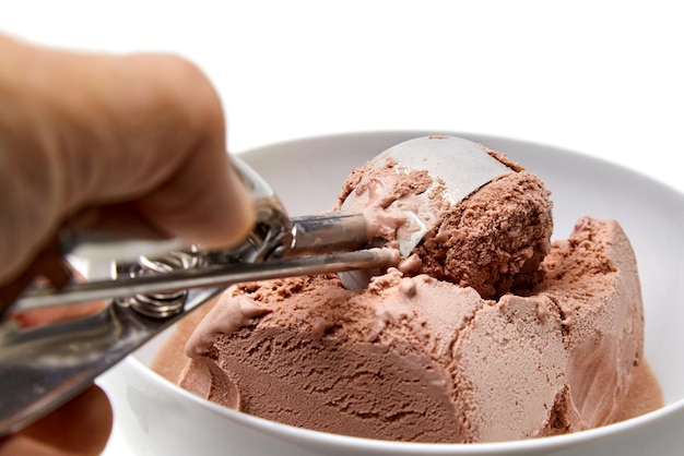 La mano de una persona con una cuchara de helado saca helado de chocolate de un tazón blanco