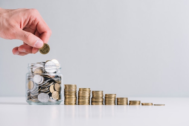 Foto la mano de una persona que pone el dinero en el tarro de cristal cerca de monedas apiladas decrecientes