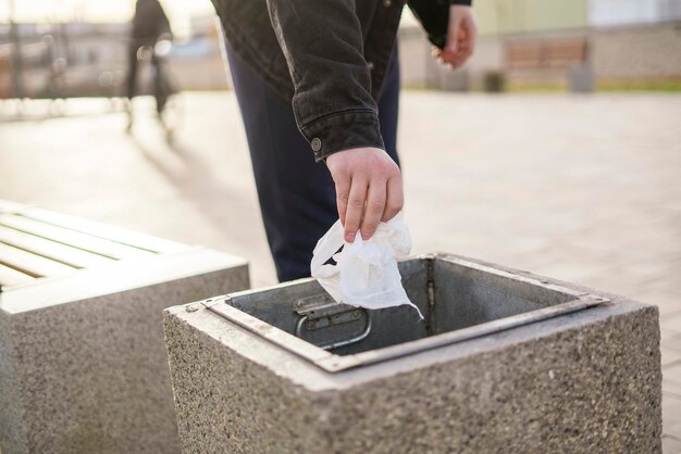 La mano de una persona tirando basura en la urna de basura al aire libre en la calle