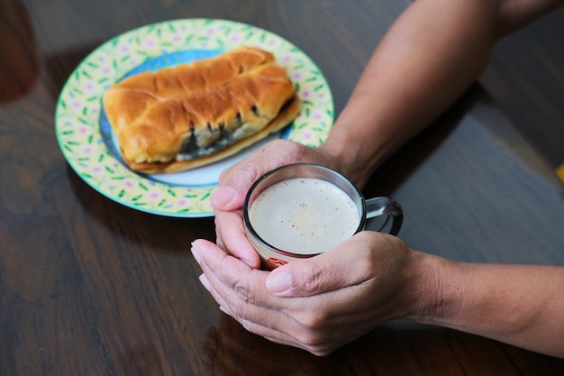 Mano de la persona tocando un vaso de café caliente con pan en un plato al lado