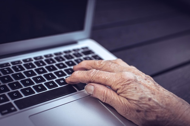 La mano de las personas mayores en el teclado de la computadora portátil