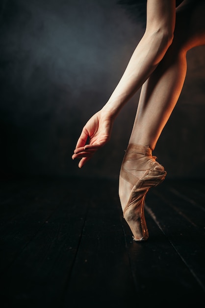 Mano y piernas de bailarina en pointes, piso de madera negra. Bailarina en vestido rojo y práctica de baile negro en el escenario del teatro