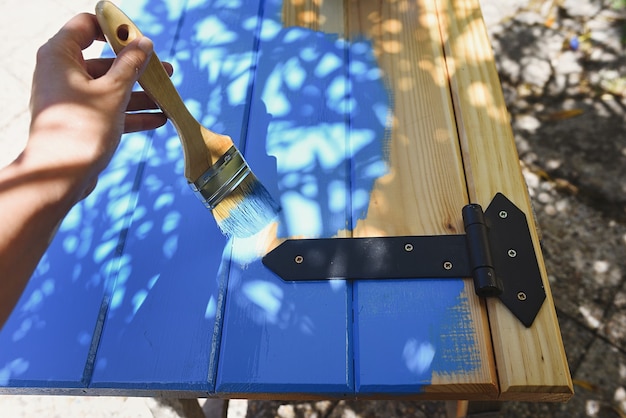 Mano con pincel pintando una contraventana de madera de pino en azul.