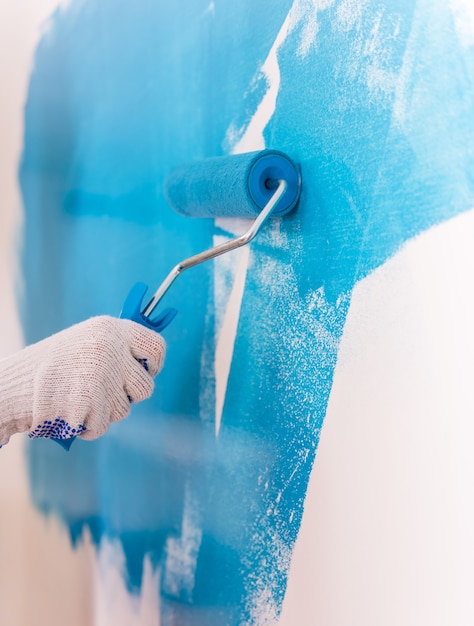 Mano pinta una pared blanca en azul claro.