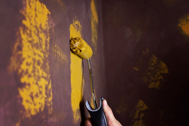 La mano del pintor está pintada de amarillo en la vieja pared marrón con espacio de copia.