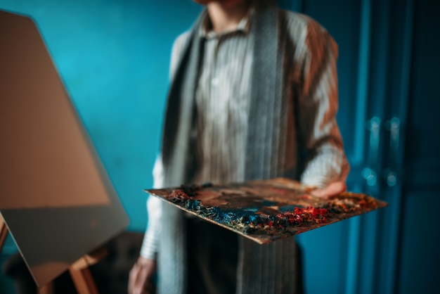 La mano del pintor masculino sostiene la paleta contra el caballete.