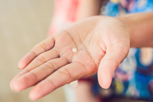 Mano con pinzas sosteniendo perlas y ostras sobre fondo de madera