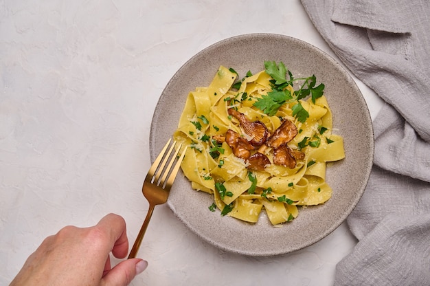 La mano plana de la mujer sostiene un tenedor dorado con pasta pappardelle con champiñones, rebozuelos, queso y