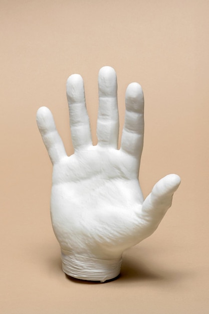 Mano de plástico impresa en 3D que muestra cinco dedos en un fondo beige