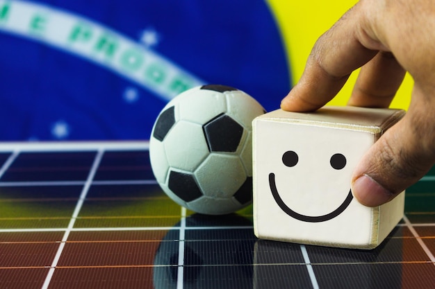 La mano pone cubos de madera con cara sonriente y cara triste y la bandera de Brasil en el panel solar fotovoltaico Concepto de mentalidad deportiva positiva