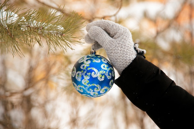 Mano poniendo adorno de bola de Navidad decorado azul en un árbol de Navidad