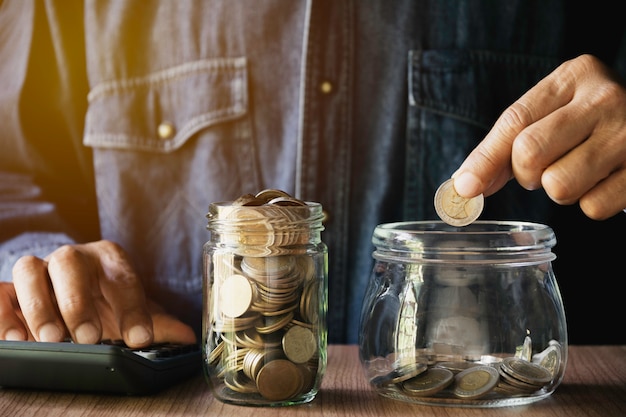 Mano poniendo dinero moneda en el frasco de vidrio. Ahorro de dinero, concepto financiero y contable.