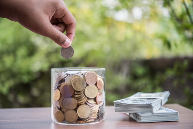 La mano poniendo monedas en el frasco con la pila de dinero paso creciente crecimiento ahorro de dinero