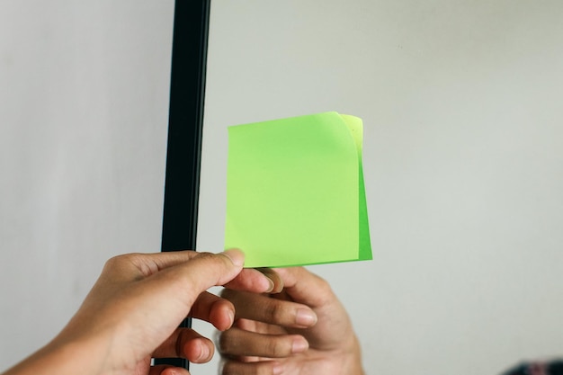 La mano poniendo notas adhesivas verdes en blanco en el espejo