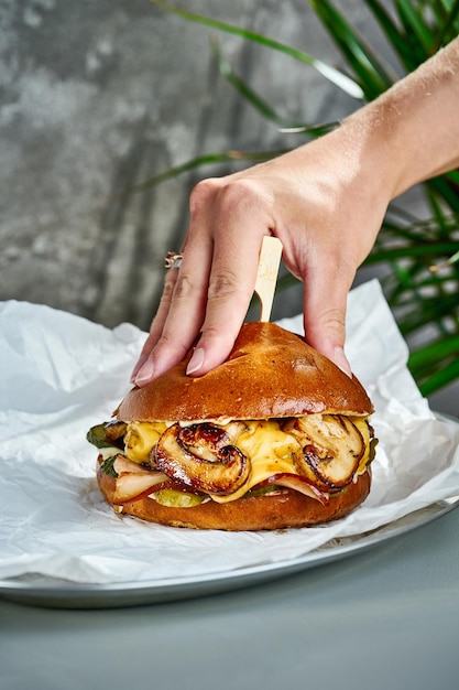 Una mano presiona una hamburguesa de pan con champiñones, queso, tocino en pergamino blanco, enfoque selectivo de primer plano