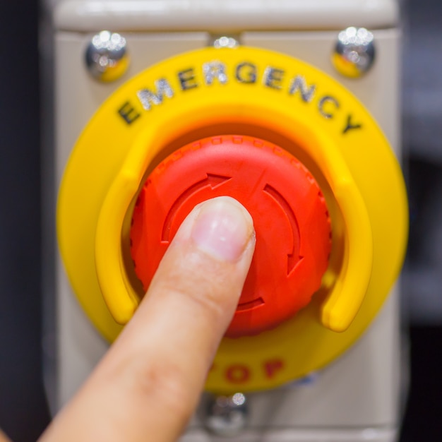 Mano presionando el botón rojo de emergencia o el botón de parada