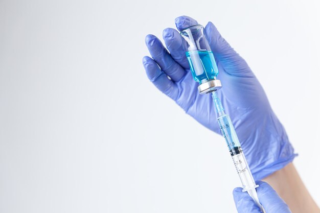 La mano del primer en guantes de goma protectores sostiene y llena la jeringa de la botella con la vacuna