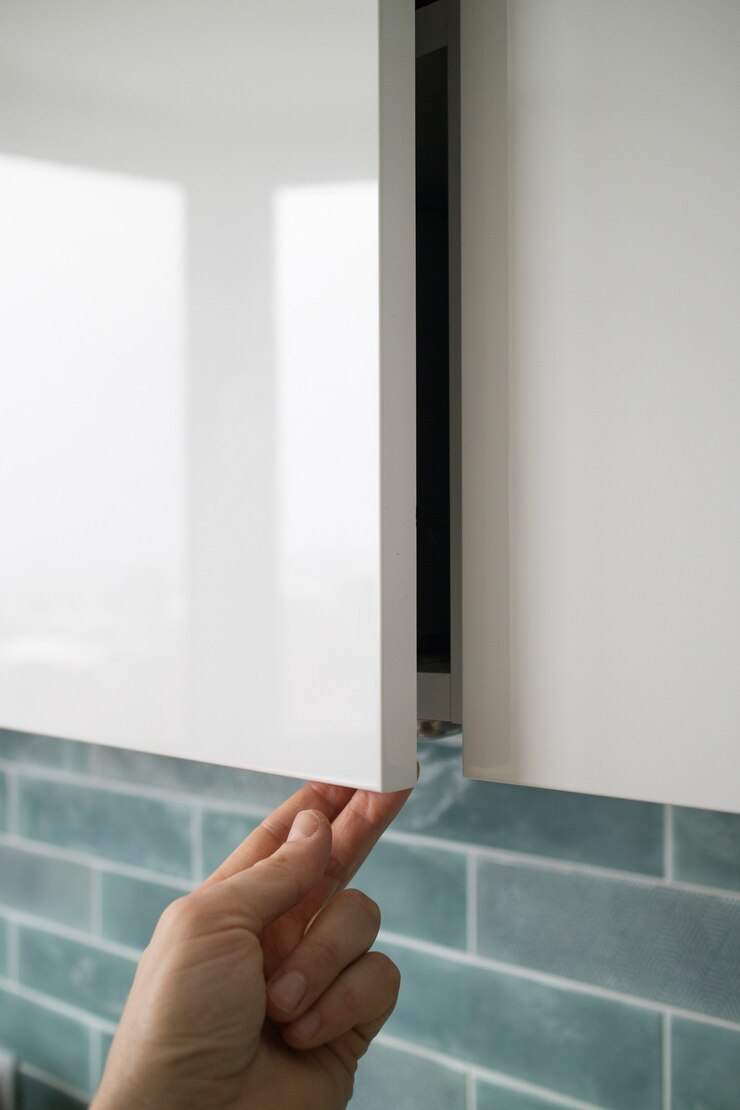 La mano del primer hombre abriendo o cerrando la puerta del armario de cocina sobre un fondo azul del interior de la cocina. Muebles de cocina modernos sin tiradores con un pequeño fondo adicional para abrir la puerta.