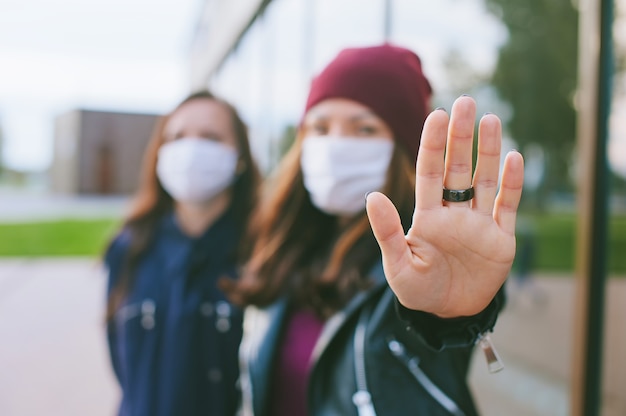 Mano en primer plano de la cámara, mujeres con máscaras médicas. Con el telón de fondo de un edificio de cristal. Detener el concepto de virus covid-19.