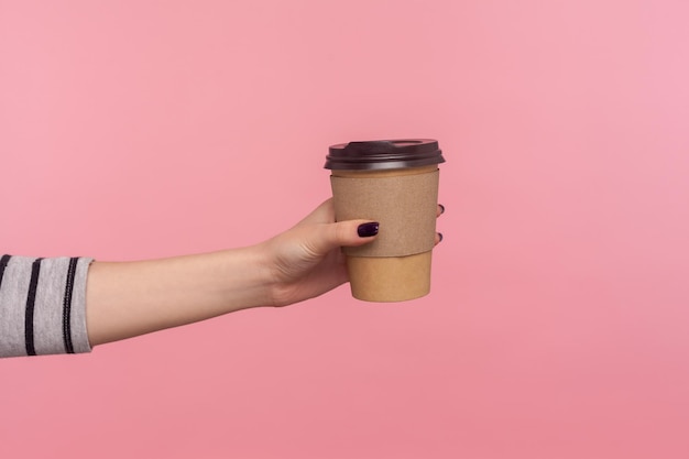 Mano de primer plano dando café en una taza desechable bebida caliente con cafeína para aumentar la energía en el descanso para tomar café de la mañana en el trabajo bebida sabrosa y sesión de estudio interior de relajación aislado en fondo rosa