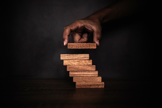 Mano de primer plano está colocando la torre de bloques de madera apilados en el escalón de la escalera